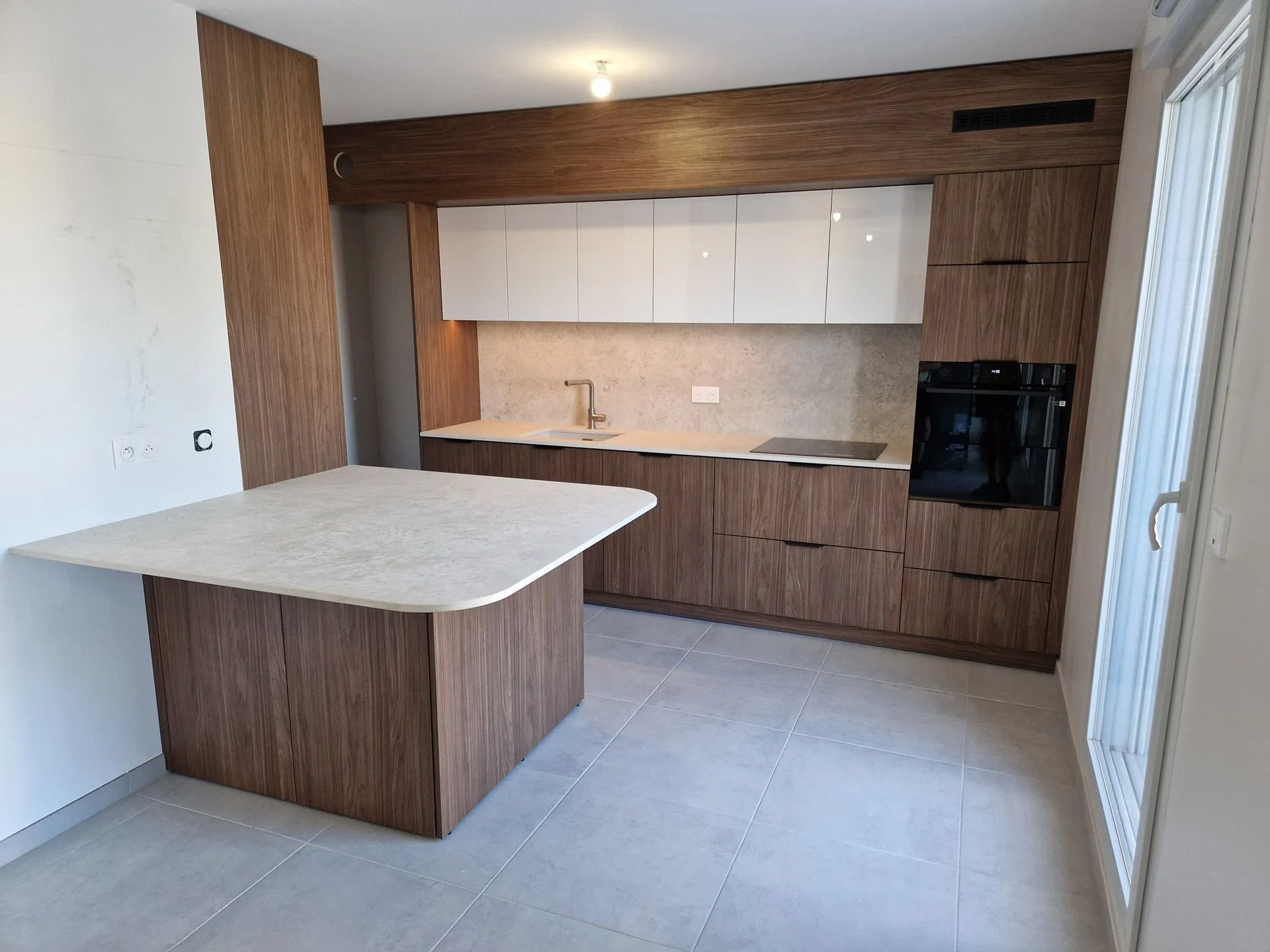 Cuisine en façades noyer avec meubles hauts blancs brillants, four encastré et îlot au plan clair aux angles arrondis